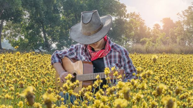 Asian farmer sitting in his bright yellow field with guitar