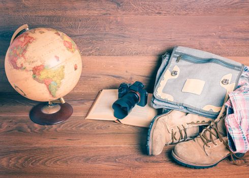 Front view of globe,camera,book,bag,boots and shirt, wooden background,vintage look for travel concept.