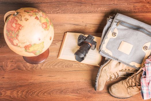 Top view of globe,camera,book,bag,boots and shirt, wooden background,vintage look for travel concept.