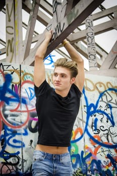 Attractive blue eyed, blond young man in black t-shirt hanging from concrete structure