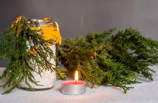 Christmas decorations on the table, hand made candle in a glass bottle with orange peel stars and fir tree branch ,tablecloth,tangerine and fir tree branch