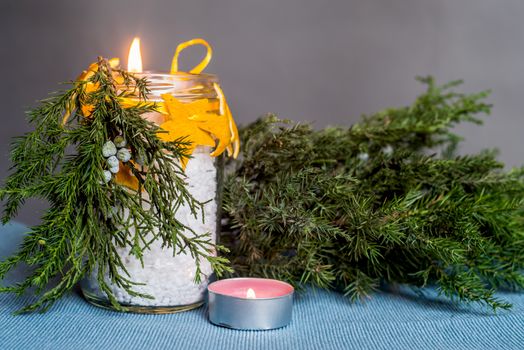 Christmas decorations on the table, hand made candle in a glass bottle with orange peel stars and fir tree branch ,tablecloth,candle and fir tree branch