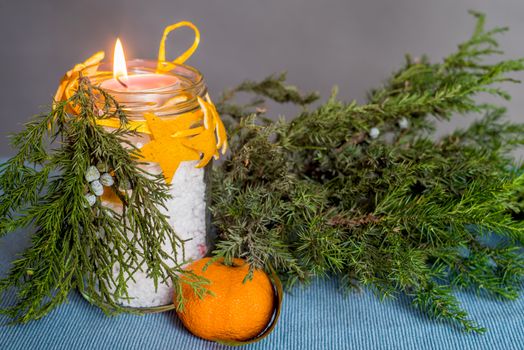 Christmas decorations on the table, hand made candle in a glass bottle with orange peel stars and fir tree branch ,tablecloth,tangerine and fir tree branch
