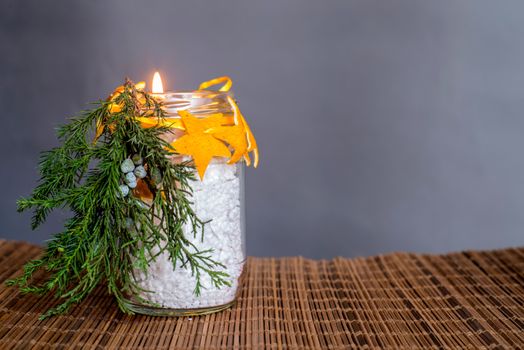 Christmas decorations on the table, hand made lit candle in a glass bottle with orange peel stars on the wooden tablecloth on grey