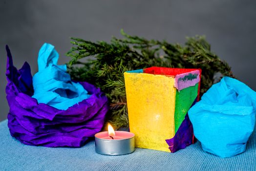 christmas craft composition on the blue tablecloth. candle with fir tree branch, crepe paper and blue tablecloth