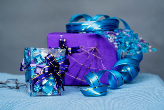 christmas craft composition on the blue tablecloth. candle with gems and blue ribbon, a gift and xmas tree decorations