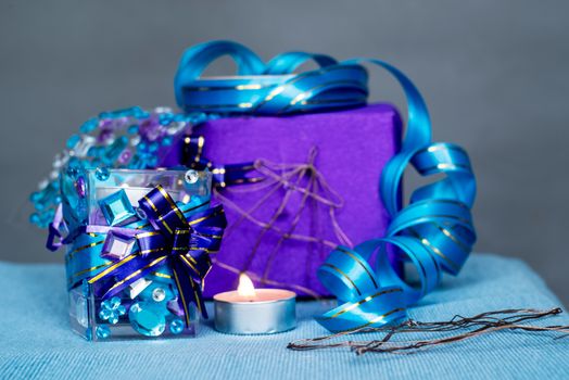 christmas craft composition on the blue tablecloth. candle with gems and blue ribbon, a gift and xmas tree decorations