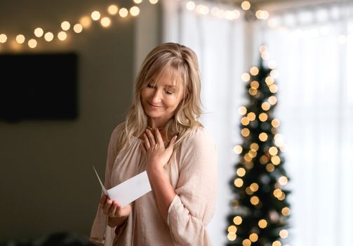 Woman reading a heartfelt message, note, book or card.   She is smiling and has her hand to heart.