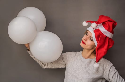 smiling womanwith red lips in santa hats with tree white balloons on grey background