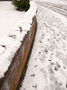 snow on brick wall and footpath with foot prints winter; essex; england; uk