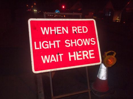red construction sign at night road when red light shows wait here traffic lights; essex; england; uk