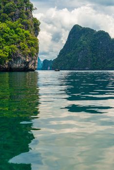 vertical photograph - a picturesque bay, view of a traditional Thai boat in the sea near the rocks