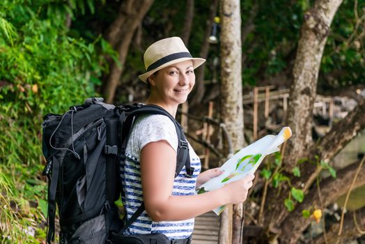 tourist in a hat with a map and a big backpack in the jungle of Asia