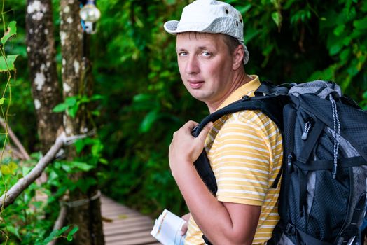 portrait of a tourist in a hat with a backpack on a background of a green jungle