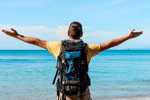 tourist with a big backpack on the beach with outstretched hands to the sides enjoy a beautiful view