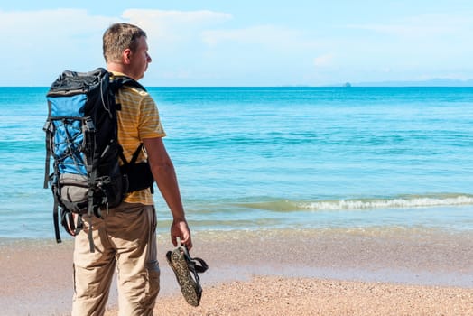 tourist with a backpack spends vacation on the beach, admires a beautiful view