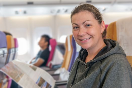 happy airplane passenger with magazine in chair smiling during flight