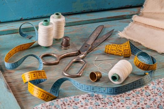 Retro sewing accessories - scissors, tape measure, thread on blue wooden background