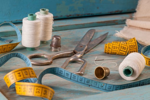 Retro sewing accessories - scissors, tape measure, thread on blue wooden background