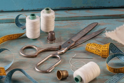 Retro sewing accessories - scissors, tape measure, thread on blue wooden background