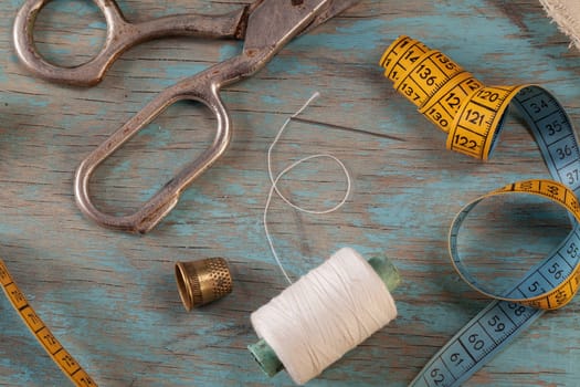 Retro sewing accessories - scissors, tape measure, thread on blue wooden background