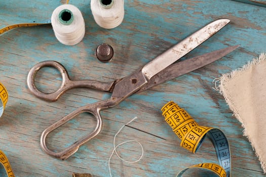 Retro sewing accessories - scissors, tape measure, thread on blue wooden background