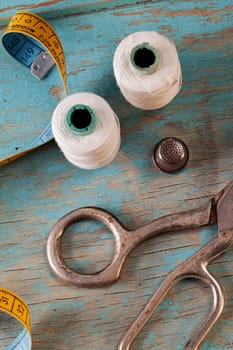 Retro sewing accessories - scissors, tape measure, thread on blue wooden background