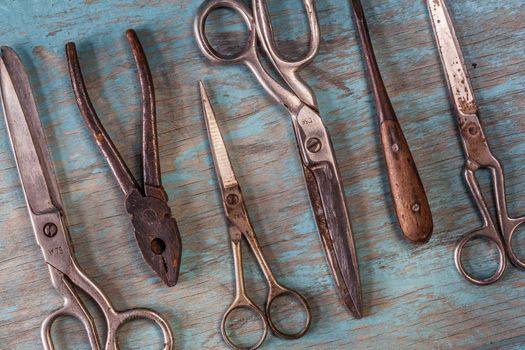 Top view on a collection of vintage tools on a blue wooden background: scissors, pliers, screwdriver. Repairing, craftsmanship and handwork concept, flat lay.