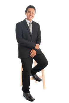 Full body portrait of young Southeast Asian businessman sitting on high chair, isolated on white background. 
