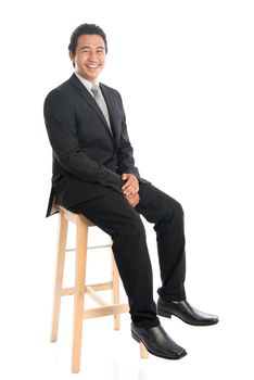 Full body portrait of handsome young Southeast Asian businessman sitting on high chair, isolated on white background. 