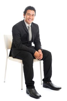 Full body portrait of attractive young Southeast Asian businessman sitting on a chair, isolated on white background. 
