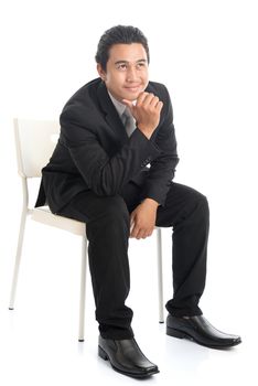 Full body portrait of attractive young Southeast Asian businessman sitting on a chair and thinking, isolated on white background. 