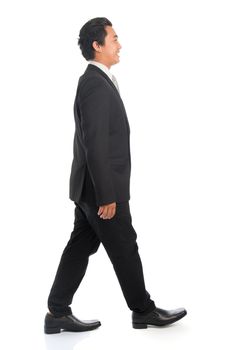 Full length side view of happy young Southeast Asian businessman walking, isolated on white background. 