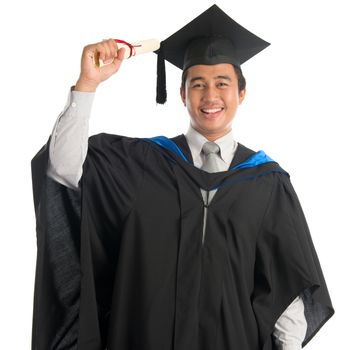 Attractive Southeast Asian male university student in graduation gown holding paper certificate, standing isolated on white background. 