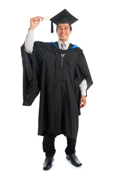 Full body attractive Southeast Asian male university student in graduation gown holding paper certificate, standing isolated on white background. 