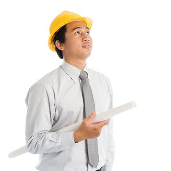 Portrait of attractive Southeast Asian engineer with yellow hard hat and blue prints looking up, standing isolated on white background.