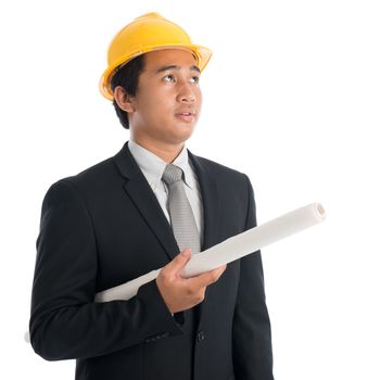 Portrait of attractive Southeast Asian engineer with yellow hard hat holding blue prints and looking away, standing isolated on white background.