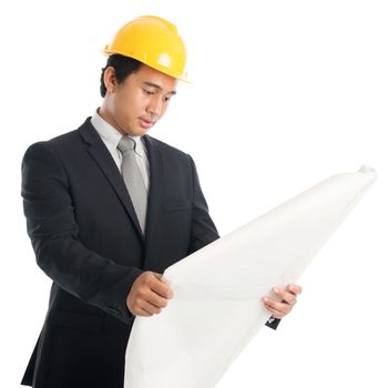 Portrait of attractive Southeast Asian engineer with yellow hard hat reading on blue prints, standing isolated on white background.