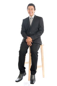 Full body portrait of happy young Southeast Asian businessman sitting on high chair, isolated on white background. 