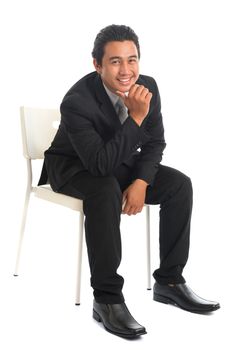 Full body attractive young Southeast Asian businessman sitting on chair, hand on chin, isolated on white background. Asian malay male model.