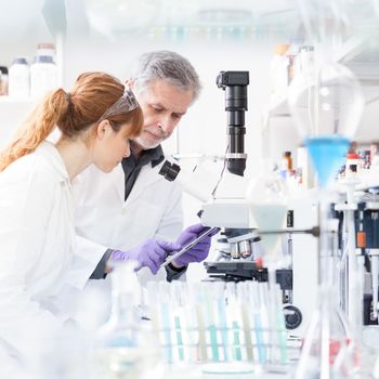 Health care researchers working in life scientific laboratory. Female research scientist and senior male supervisor looking focused at tablet computer screen evaluating and analyzing microscope image.