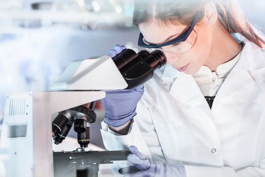 Life scientists researching in laboratory. Attractive female young scientist microscoping in their working environment. Healthcare and biotechnology.