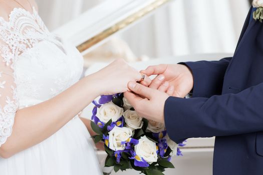 Wedding day. The groom places the ring on the bride's hand.