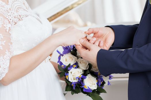 Wedding day. The groom places the ring on the bride's hand.