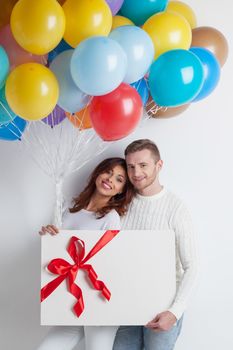 Young smiling couple with balloons and big gift box