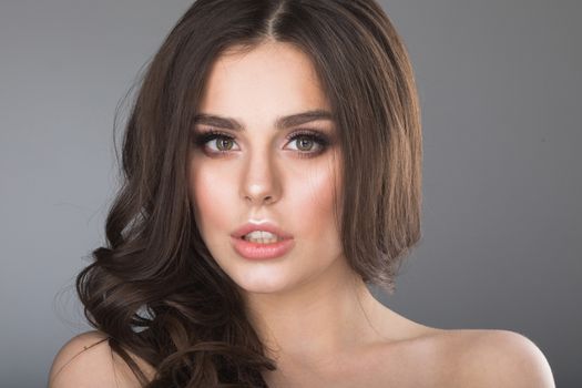 Beautiful woman with long wavy brown hair. Closeup beauty portrait of a fashion model posing at studio on gray background