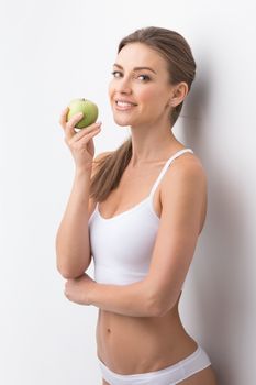 Young attractive sporty woman in white underwear holding green apple