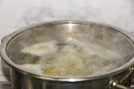 Boiling water in a pan with potatoes in the kitchen with smoke. Close up