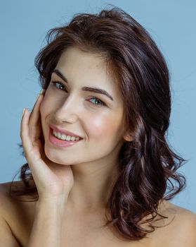 Portrait of a beautiful woman with perfect skin and dark curly hair touching face, skincare concept