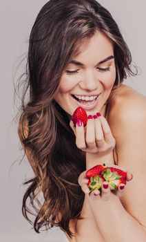 Studio portrait of a pretty girl with wavy fair hair and natural make-up eating strawberry